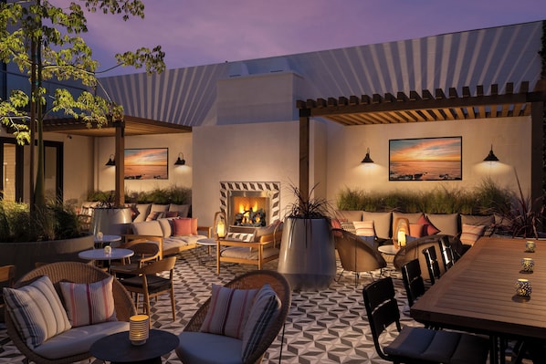 An outdoor patio area with seating arrangements, a fire feature, and ambient lighting.