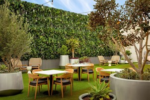 Un patio con varias mesas y sillas, rodeado de abundante follaje y una diversidad de plantas.