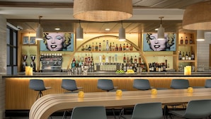 Uma área de bar com uma mesa de madeira comprida, vários banquetes e uma variedade de garrafas de bebidas e copos.