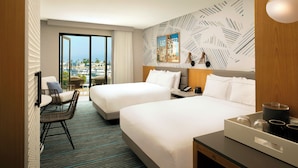 Quarto de hotel com duas camas, vista para a cidade, área de refeições e uma grande janela.