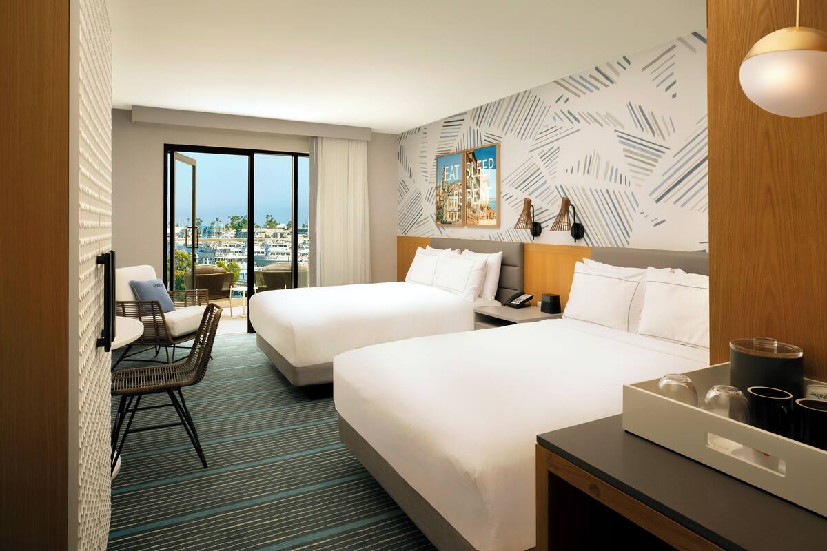 A hotel room with two beds, a view of the city, a dining area, and a large window.