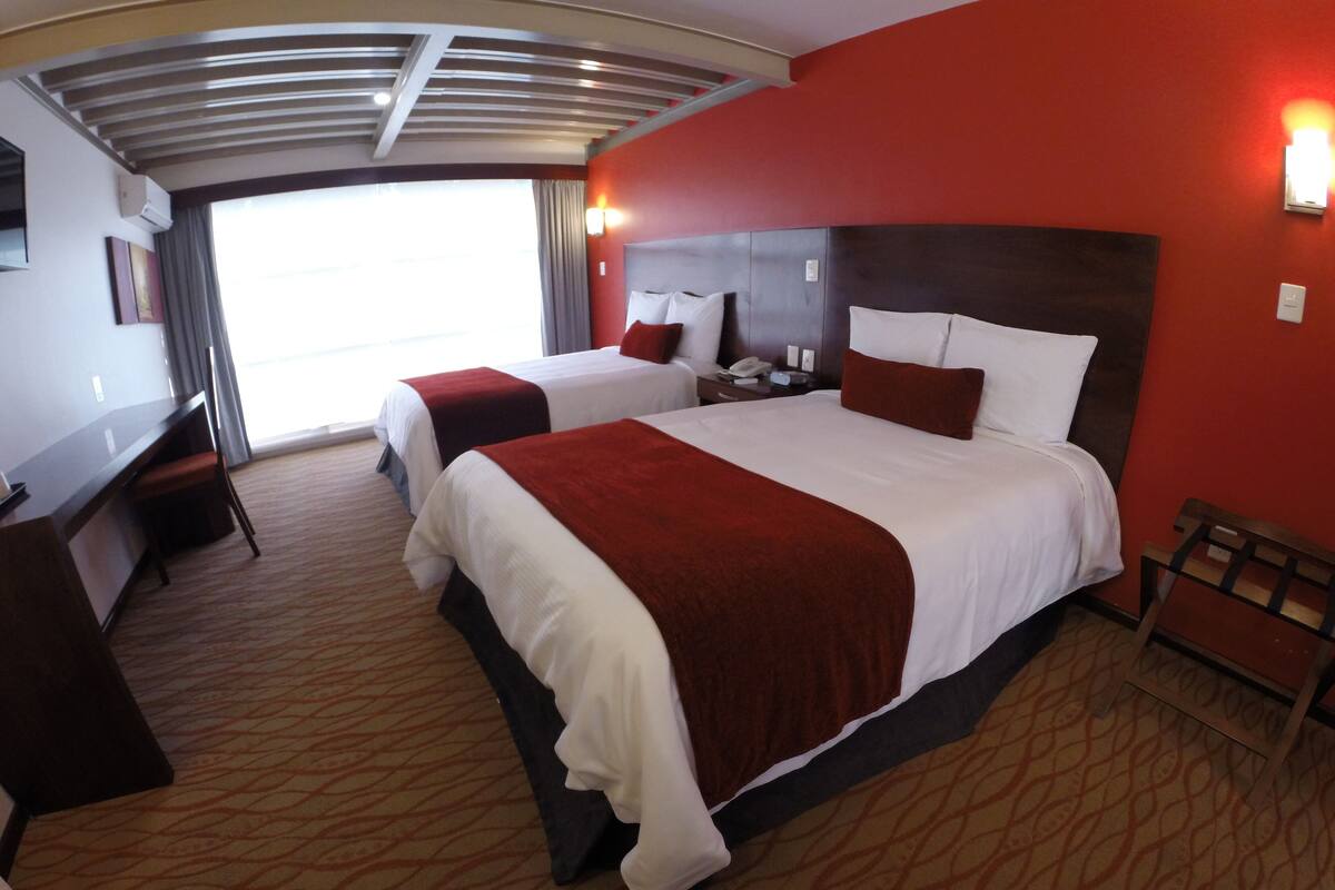 A hotel room with two beds, a desk, and a chair.