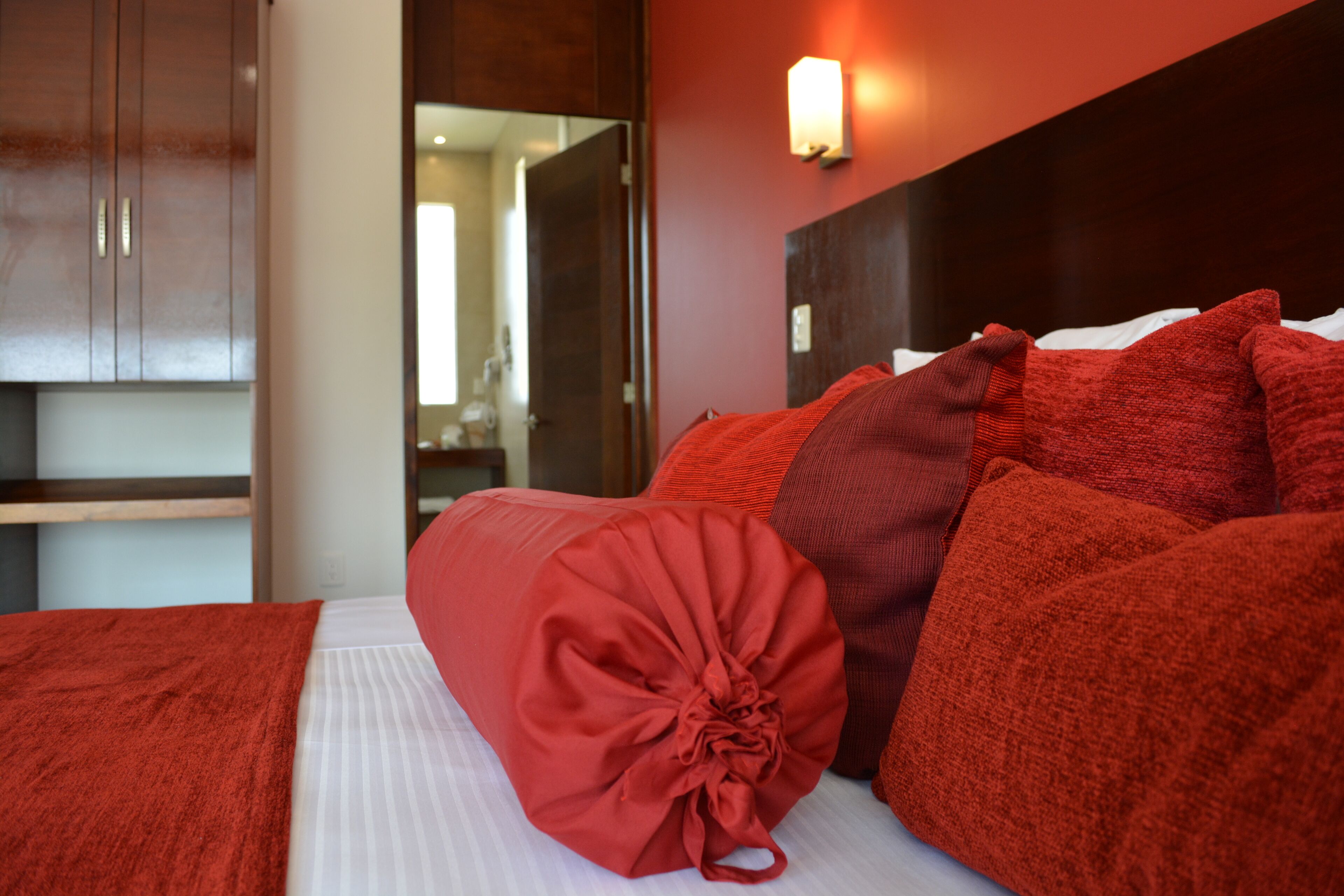 A hotel room with a bed, red bedding, a wooden headboard, and a mirror.