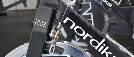 A stationary bike with "Nordika" branding and a "NK" label, in a gym setting with exercise equipment in the background.