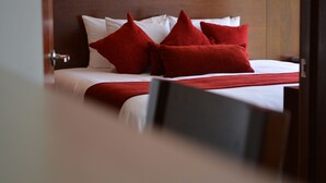 A neatly made bed with white linens and red pillows, a wooden headboard, and a visible door handle. - HS Hotel (Tepeapulco)