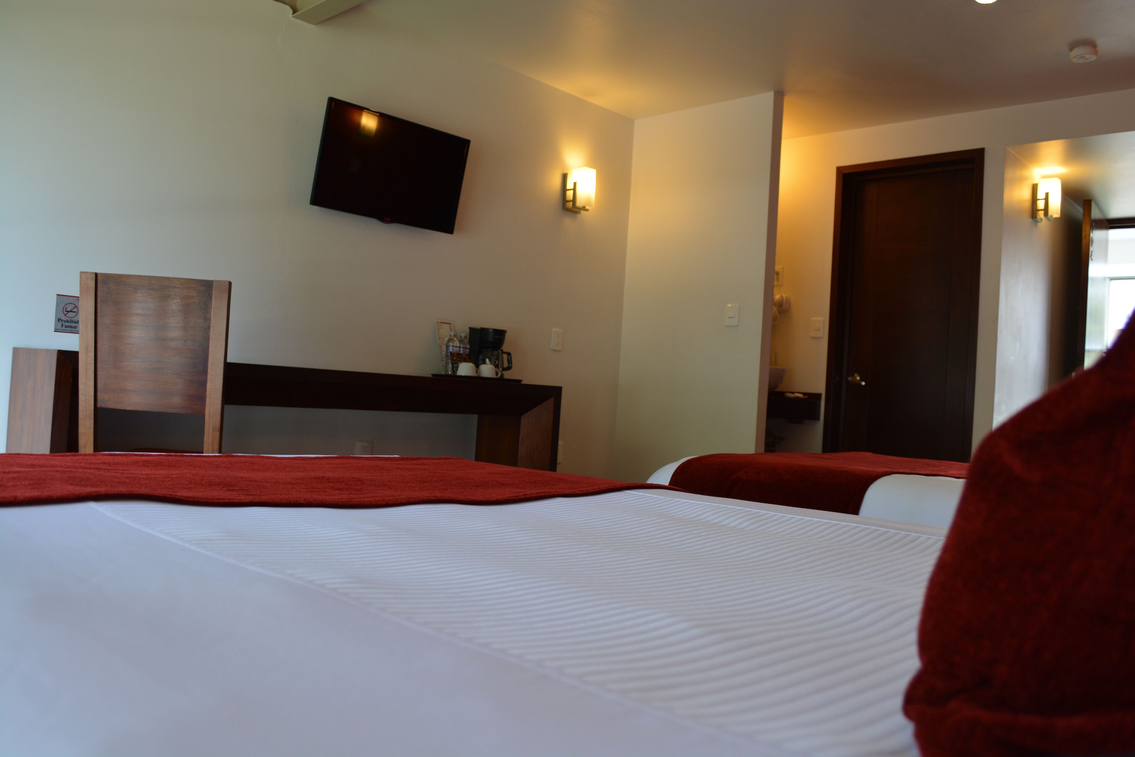 Ein Hotelzimmer mit zwei Betten, einem an der Wand montierten Fernseher und einem Schreibtisch mit Kaffeemaschine.