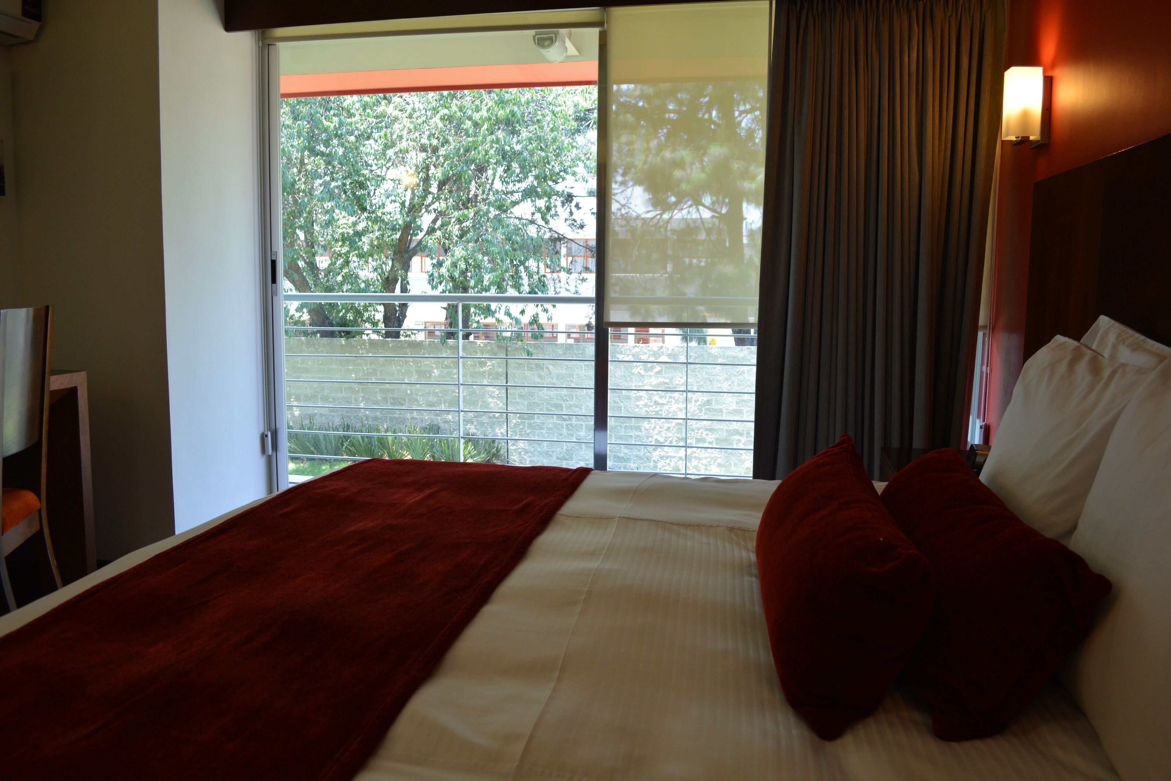 Habitación de hotel con una cama grande, una colcha roja y vistas a un balcón con barandilla.