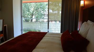 Habitación de hotel con una cama grande, una colcha roja y vistas a un balcón con barandilla.