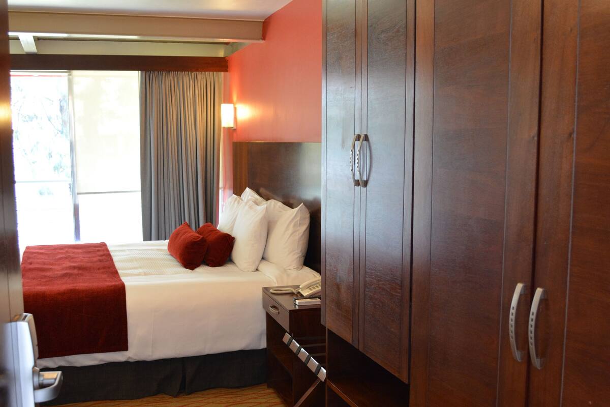 A hotel room with a large bed, a wardrobe, a desk, and a window with curtains.