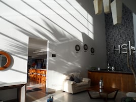 Um lobby de hotel moderno com um sofá, uma mesa de centro e um balcão de recepção. Há relógios indicando diferentes fusos horários e uma grande obra de arte abstrata na parede.