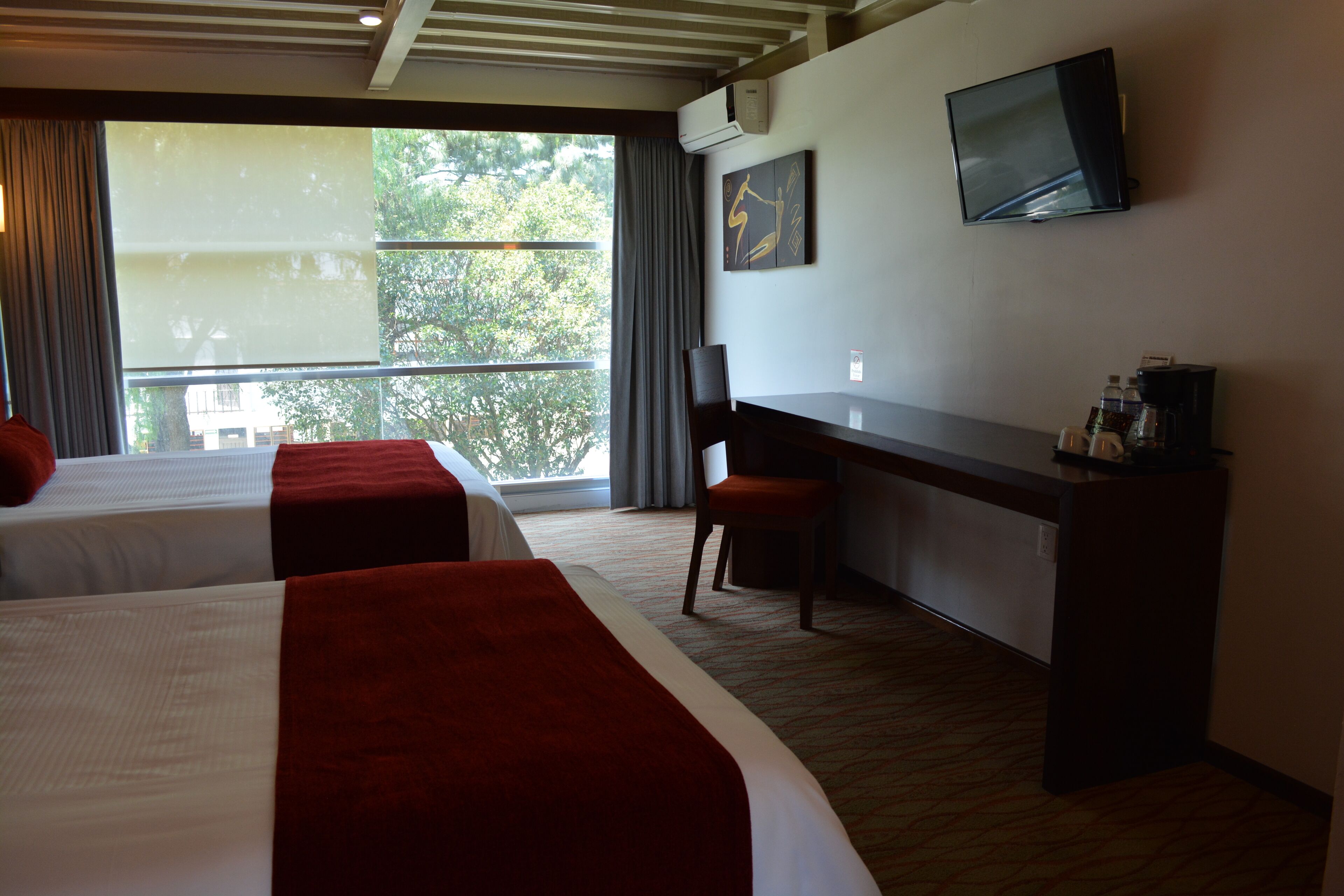 A hotel room with two beds, a desk, a chair, a TV, and a window with curtains.