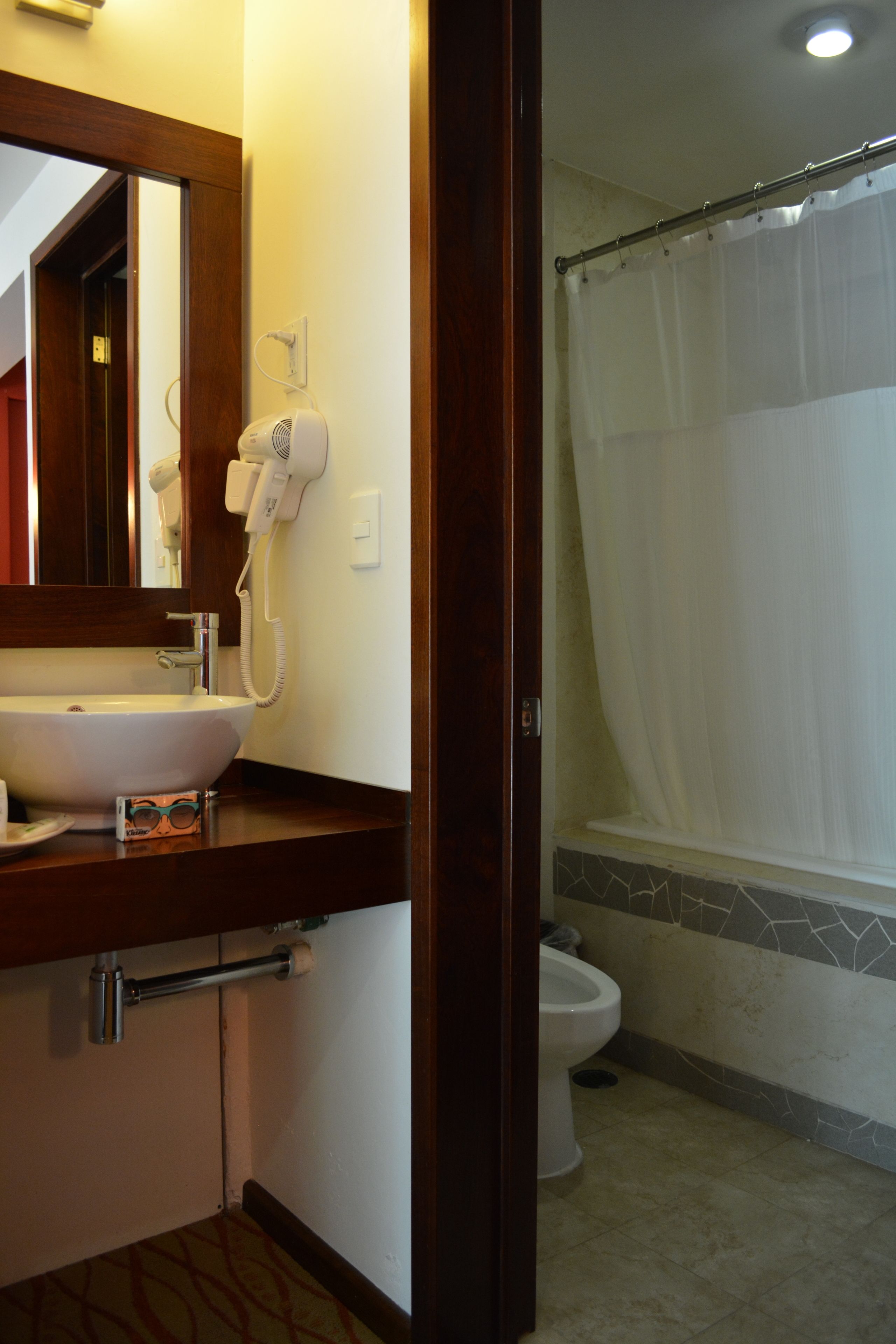 A bathroom with a sink, a hairdryer, a toilet, and a shower curtain.