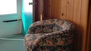 A corner room with a wooden wall, a door, and a patterned armchair. - Chapel Hill Motel (Moran)