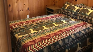 A room with wooden walls, a bed with patterned bedding, and a small wooden nightstand. - Chapel Hill Motel (Moran)