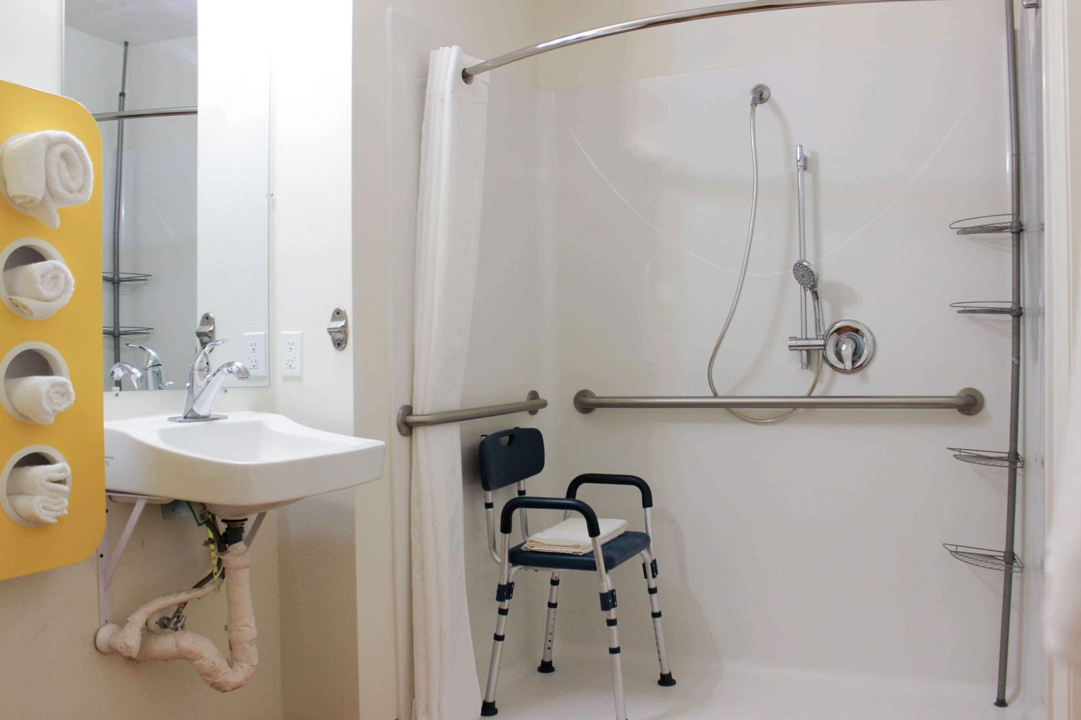Un baño con ducha, lavamanos y silla de ruedas.