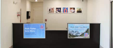 Un área de recepción con un mostrador negro, un extintor y una pared con cuadros y carteles promocionales.