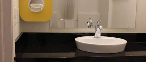 Un baño con lavamanos blanco, encimera negra y un toallero amarillo con cuatro toallas blancas.