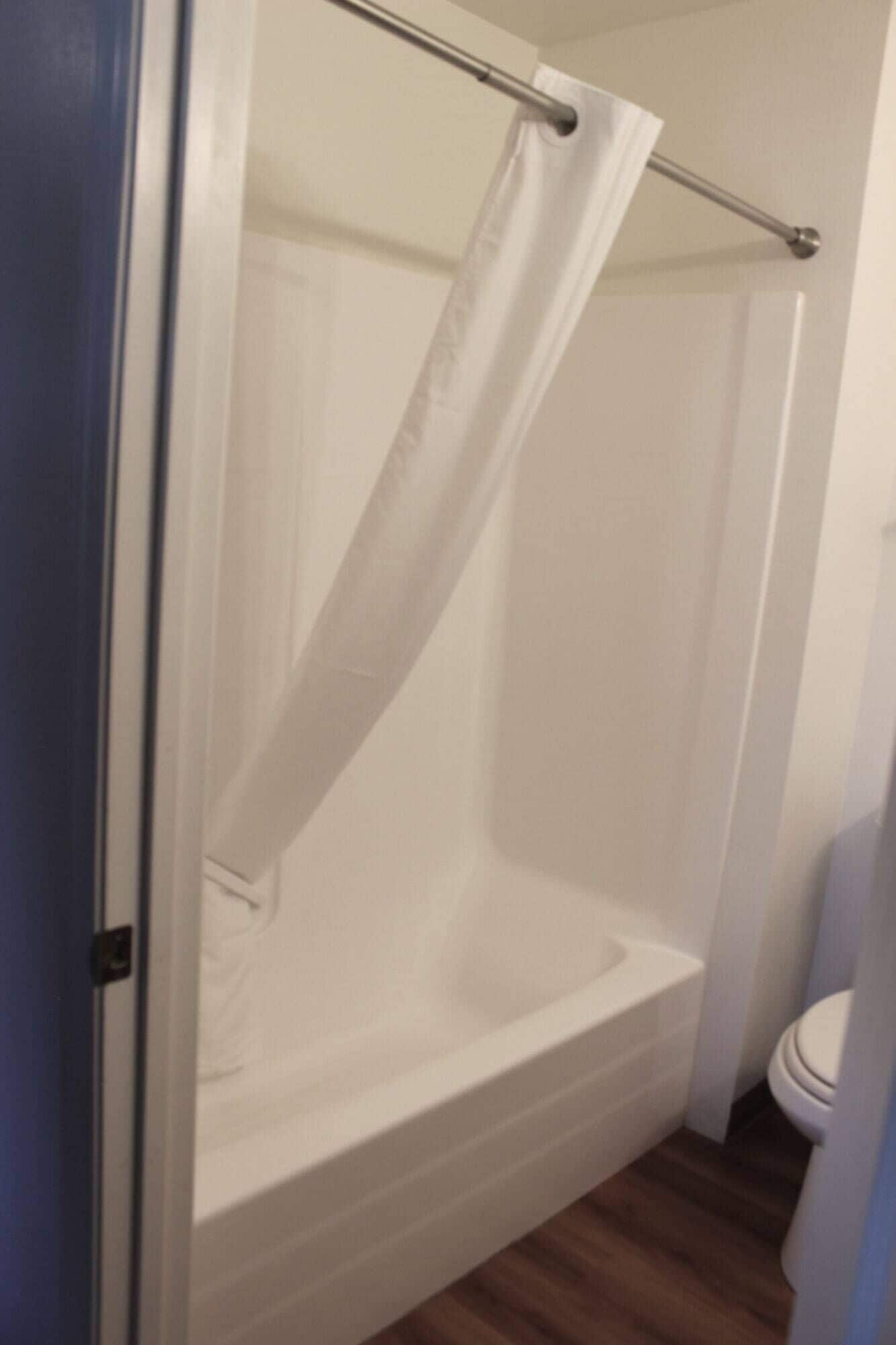 A bathroom with a white bathtub, a shower curtain, and a toilet.