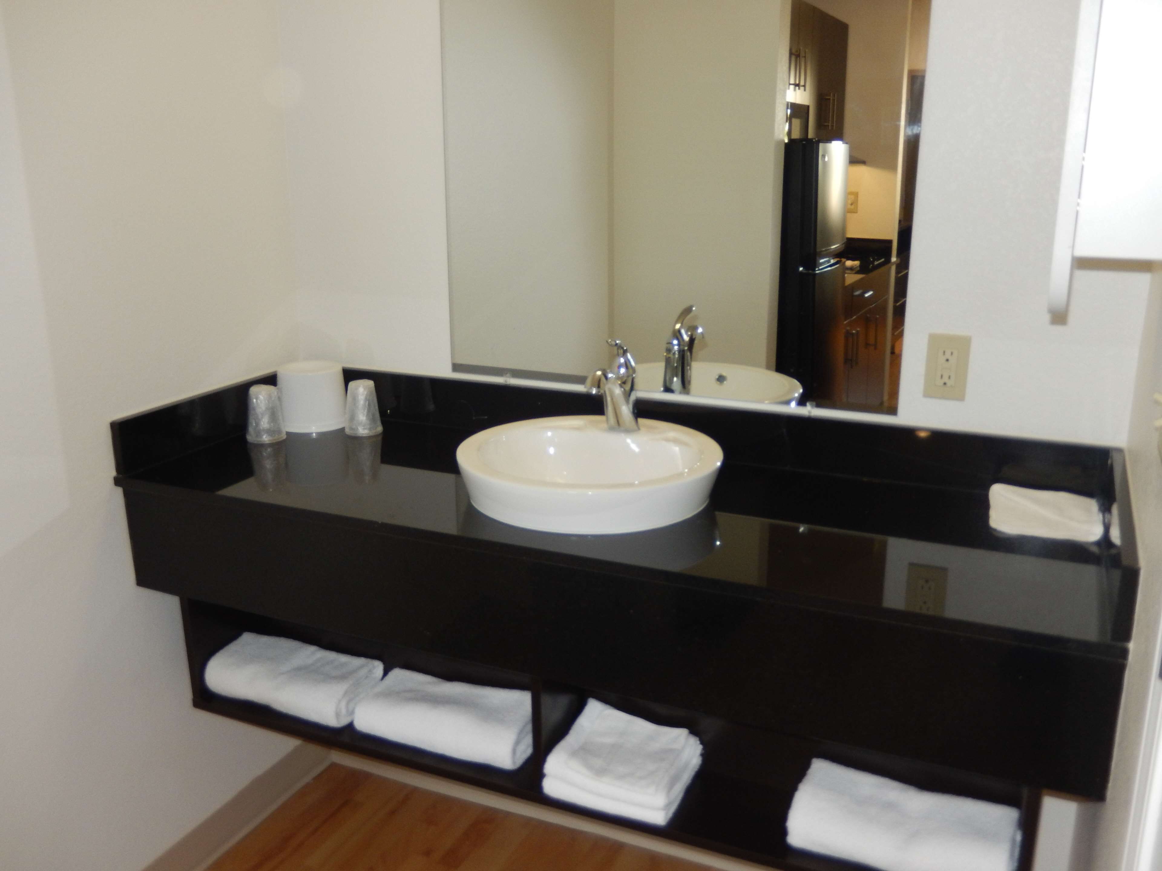 A modern bathroom with a black countertop, a white sink, and a mirror. There are towels neatly folded on the countertop.