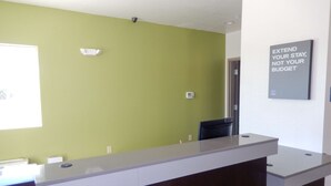 A reception desk with a green wall, a sign that reads "EXTEND YOUR STAY, NOT YOUR BUDGET", and a security camera. - Studio 6 Yukon, OK (Yukon)