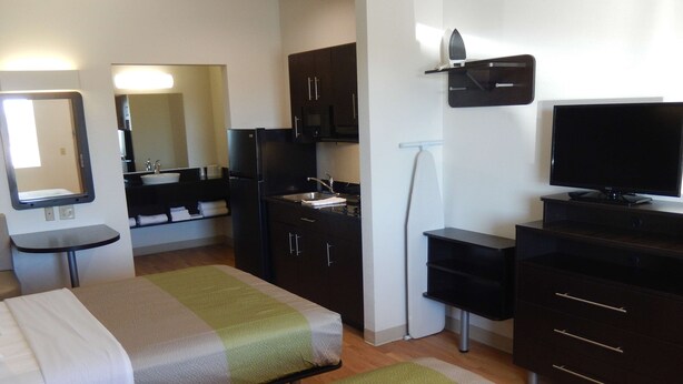A hotel room with two beds, a small table, a TV, a microwave, and a sink. - Studio 6 Yukon, OK (Yukon)