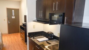 A compact kitchen with dark wooden cabinets, a black microwave, a stainless steel sink, and a black refrigerator. - Studio 6 Yukon, OK (Yukon)