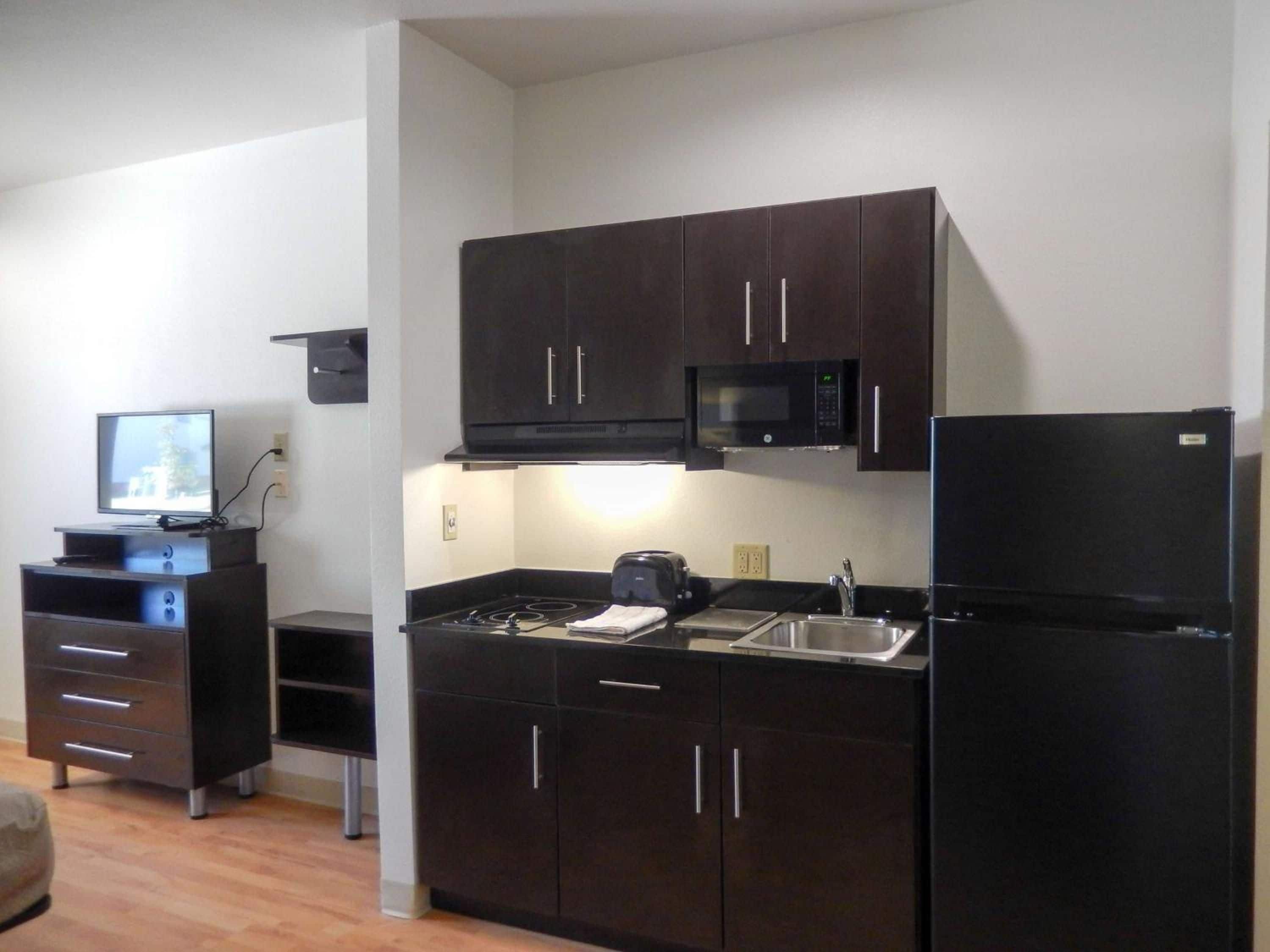 A compact kitchen with dark cabinets, a microwave, a refrigerator, a stove, and a sink.