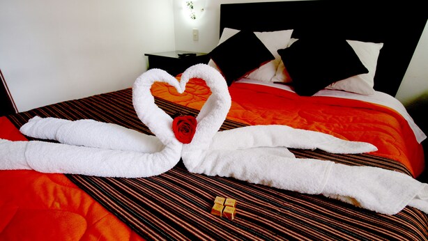 A bed with a heart-shaped towel arrangement and a single rose. - Hotel Peru Real (Cusco)