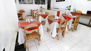 A dining area with wooden tables and chairs, white tablecloths, and a kitchen counter with various items. - Hotel Peru Real (Cusco)