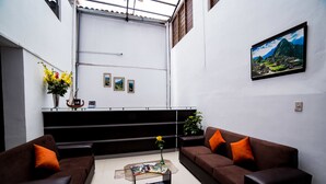 A modern living room with two brown sofas, a glass coffee table, and a vase with flowers. There are framed pictures on the wall and a painting above the sofa. - Hotel Peru Real (Cusco)