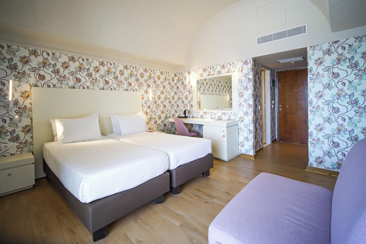 Ein Hotelzimmer mit zwei Betten, einem Schreibtisch, einem Spiegel und einem Kleiderschrank.