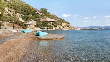 A beach with clear water, a rocky shoreline, and a pier extending into the sea.