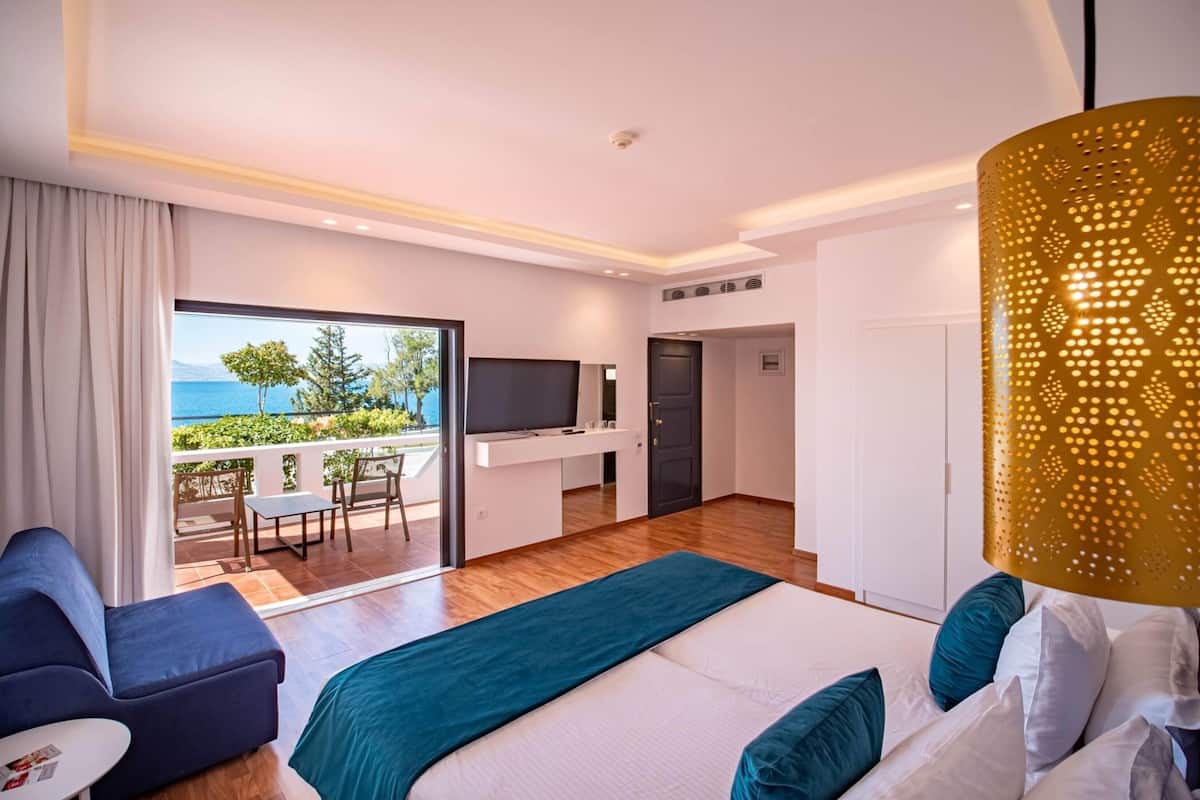 Ein Hotelzimmer mit Bett, Fernseher, einem Balkon mit Meerblick und einem Schreibtisch mit Stuhl.