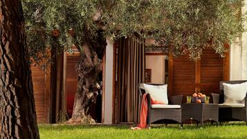 A well-maintained outdoor area with a large tree, a wicker sofa with cushions, and a wooden fence.