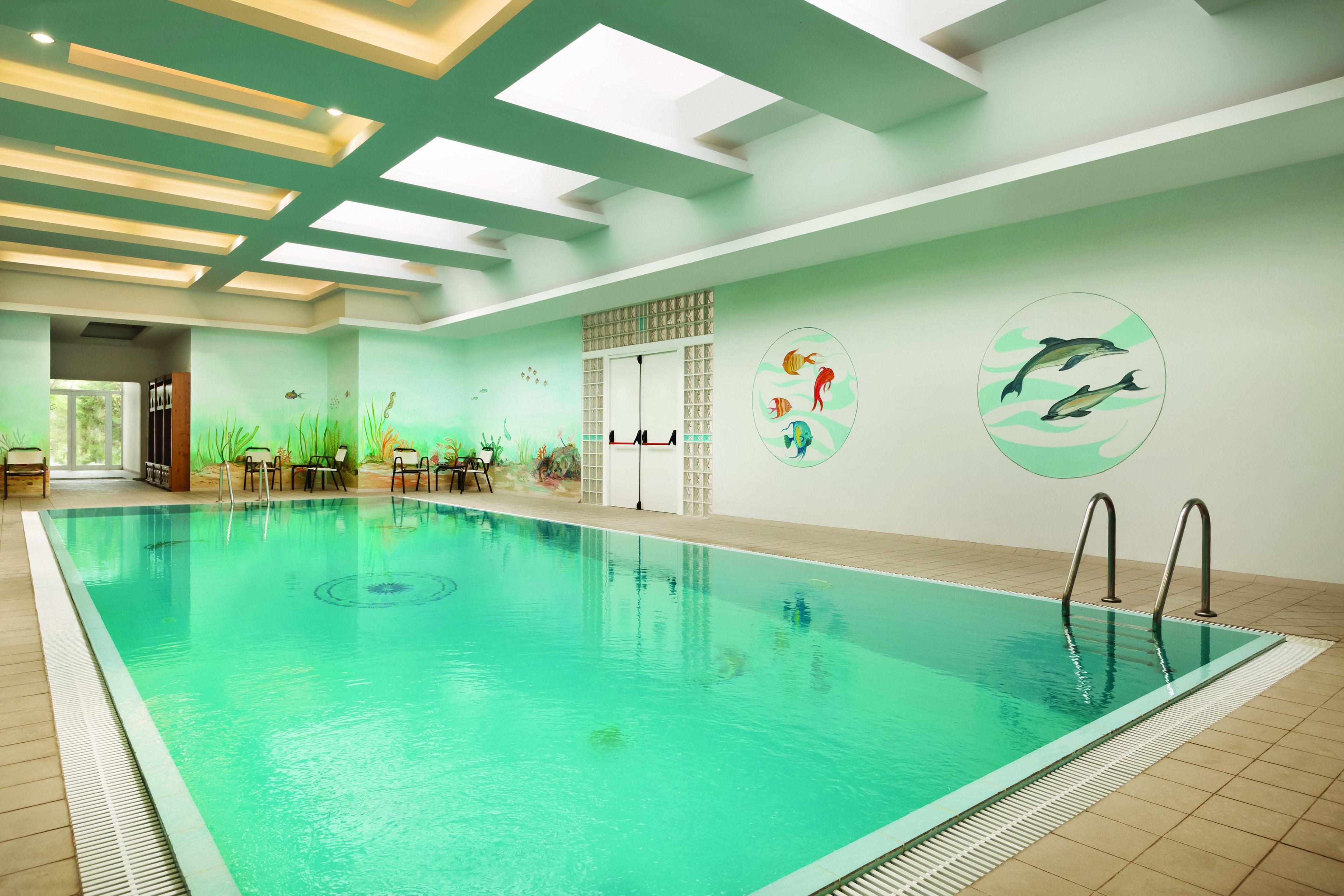 An indoor swimming pool with clear water, a tiled floor, and a ceiling with skylights.