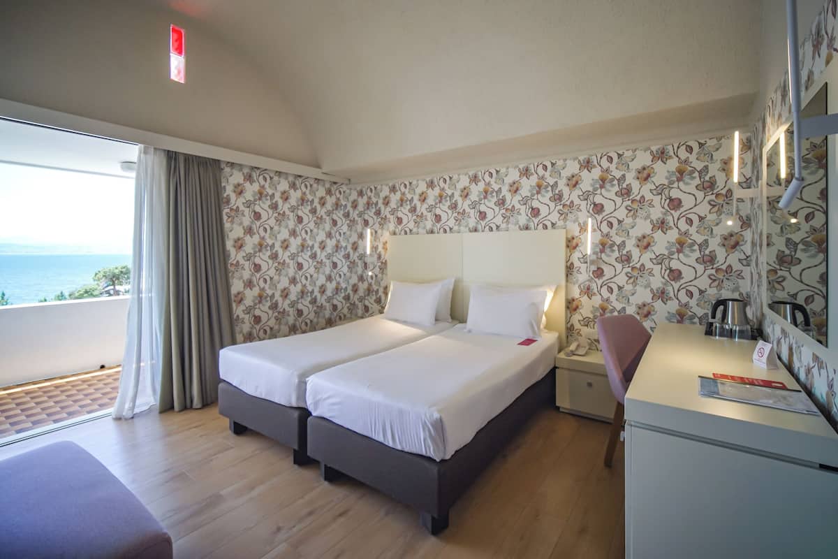 Ein Hotelzimmer mit zwei Betten, einem Schreibtisch und Meerblick.