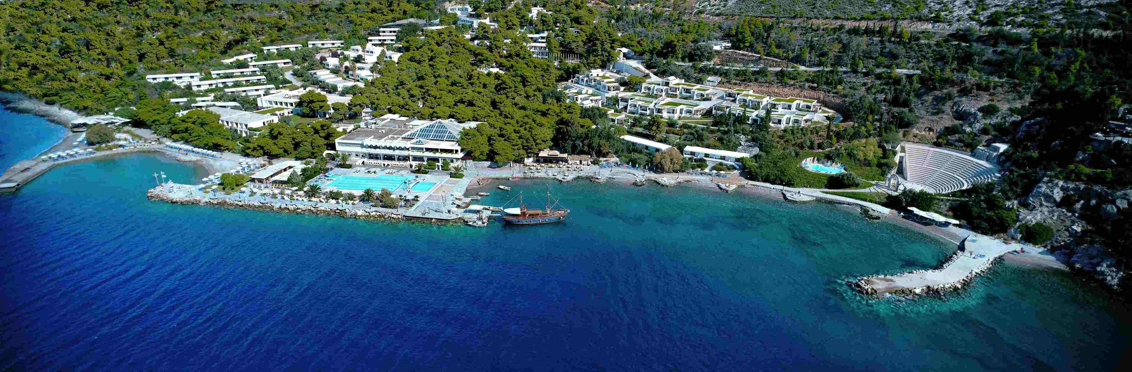 An aerial view of a coastal resort with multiple buildings, a swimming pool, and a dock with boats.
