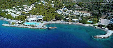 An aerial view of a coastal resort with multiple buildings, a swimming pool, and a dock with boats.