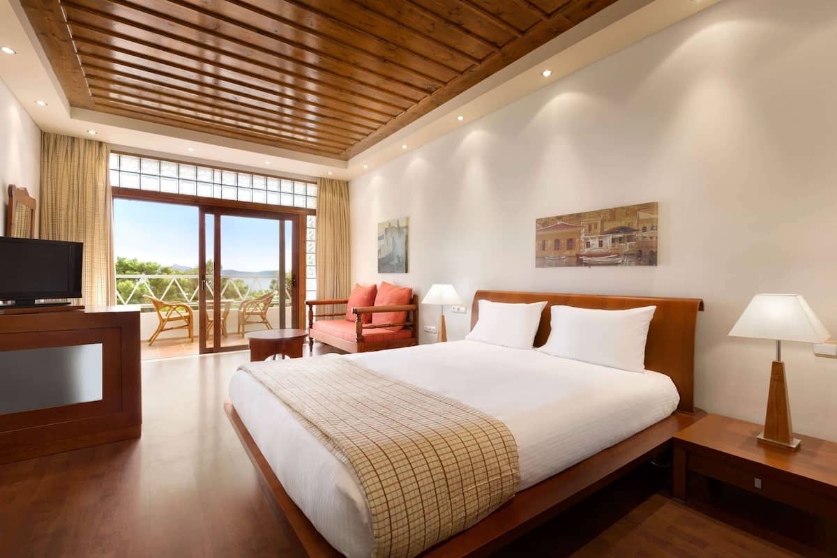 Ein Hotelzimmer mit einem großen Bett, einem Fernseher, einem Schreibtisch und einem Balkon mit Aussicht.