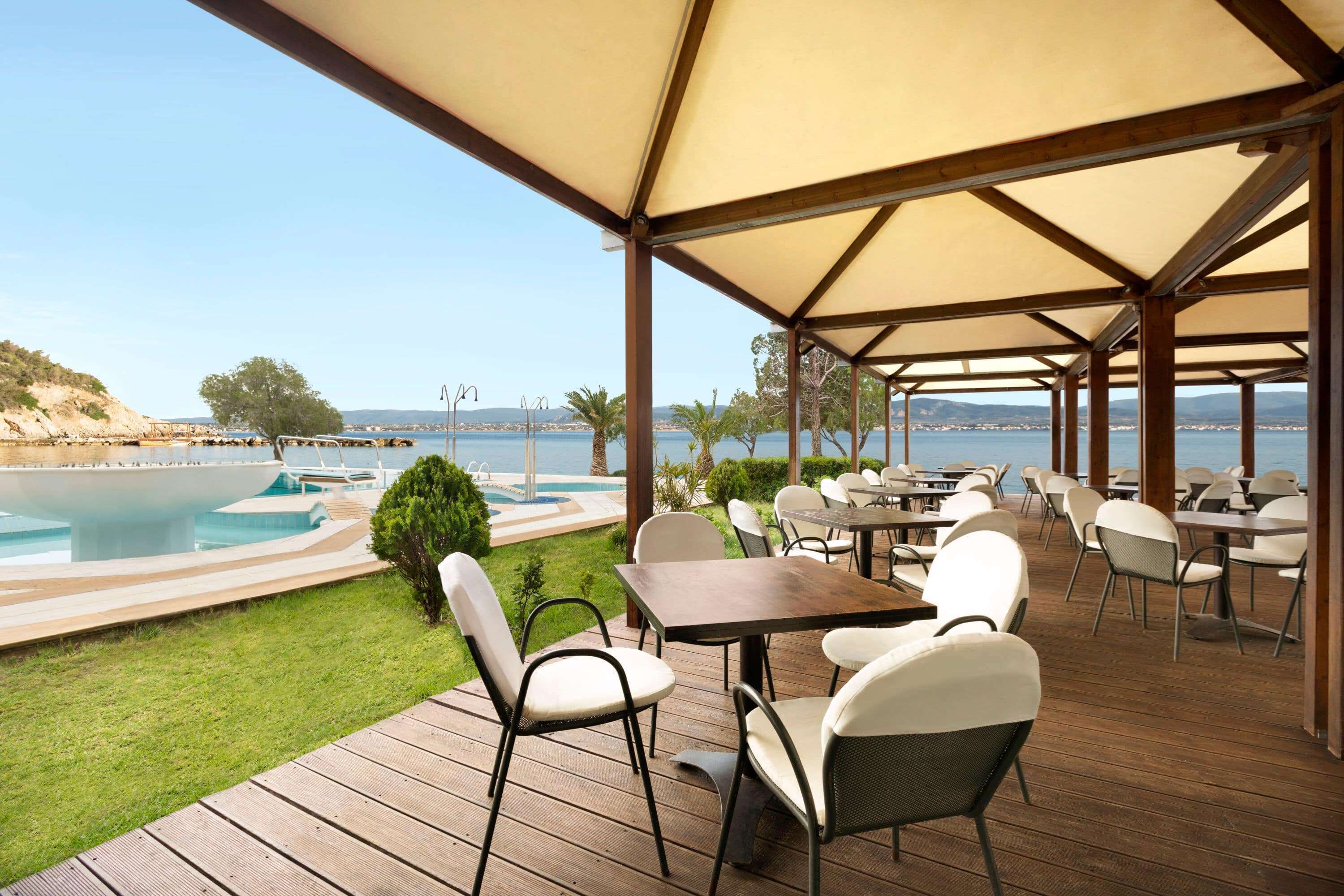 An outdoor seating area with tables and chairs, overlooking a pool and the sea.