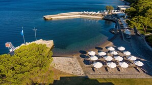 A coastal resort with a clear blue sea, a rocky beach, and a row of sun loungers with umbrellas.