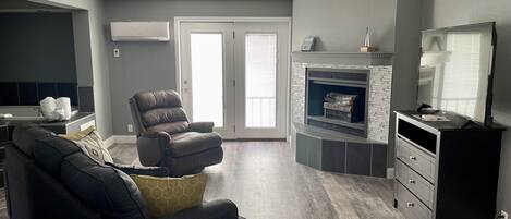 Una sala moderna con un sofá de cuero oscuro, un sillón reclinable y una chimenea.
