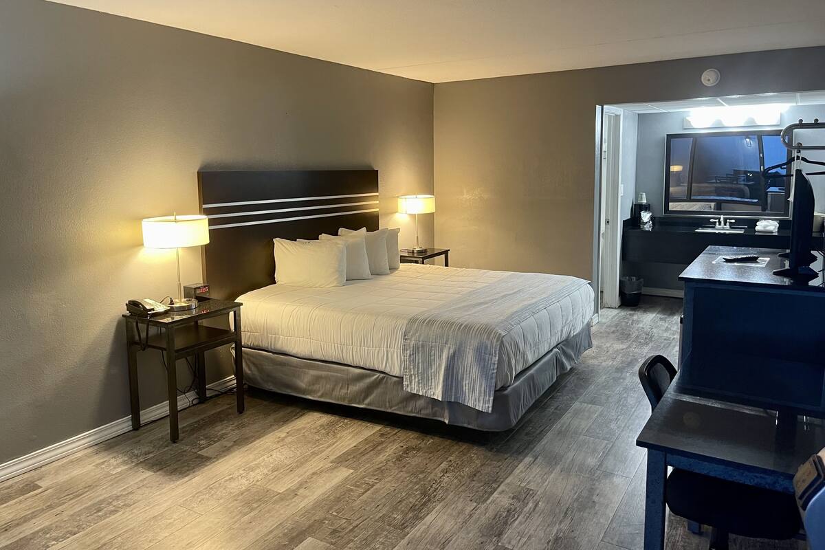 A hotel room with a bed, bedside lamps, a desk, and a television.