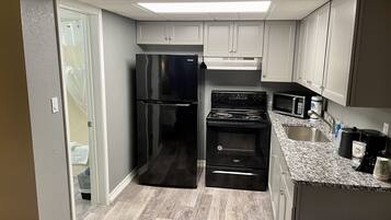 A compact kitchen with a refrigerator, stove, microwave, and sink.