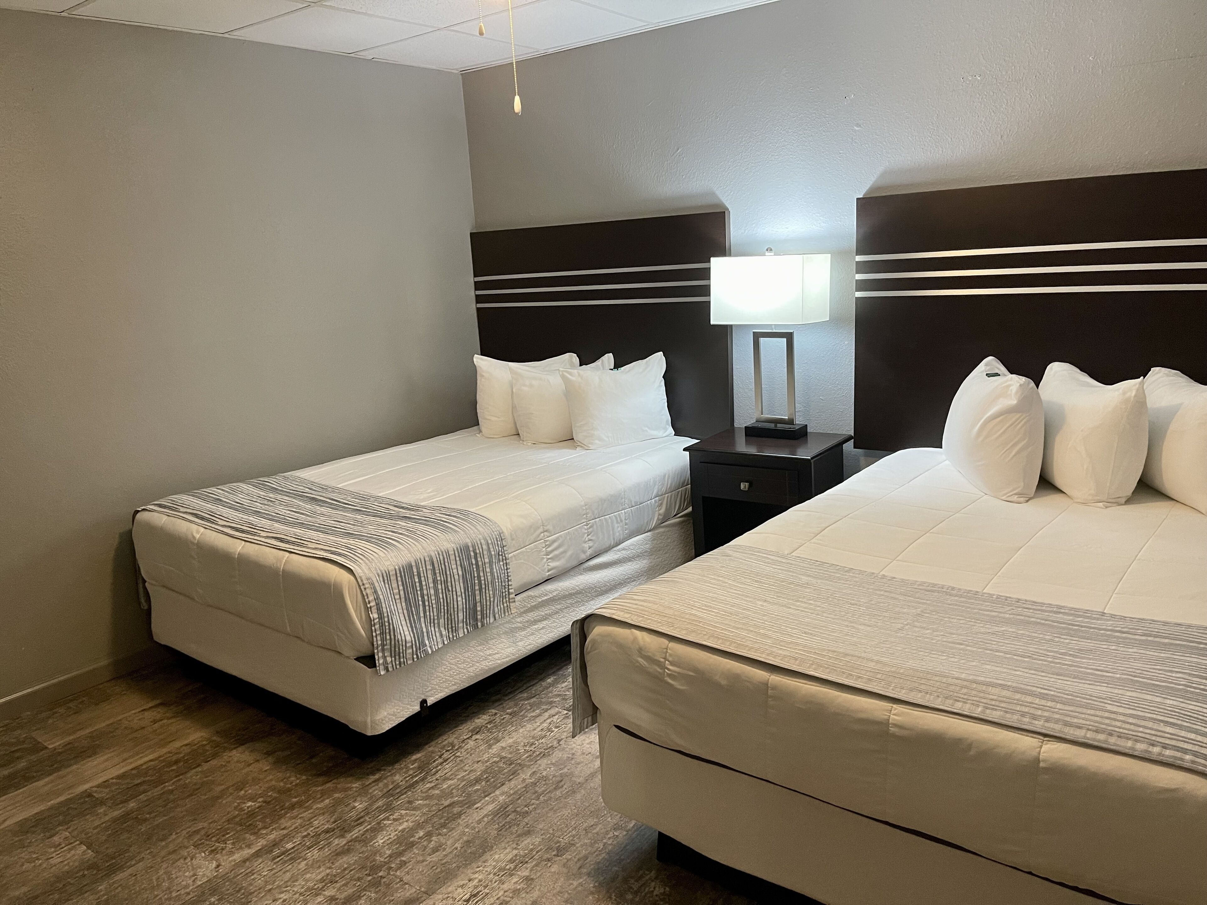 A hotel room with two beds, a nightstand with a lamp, and a wooden floor.