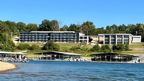 Un hotel junto al lago con varias construcciones, incluyendo un edificio grande de varios pisos y zonas cubiertas más pequeñas con asientos.