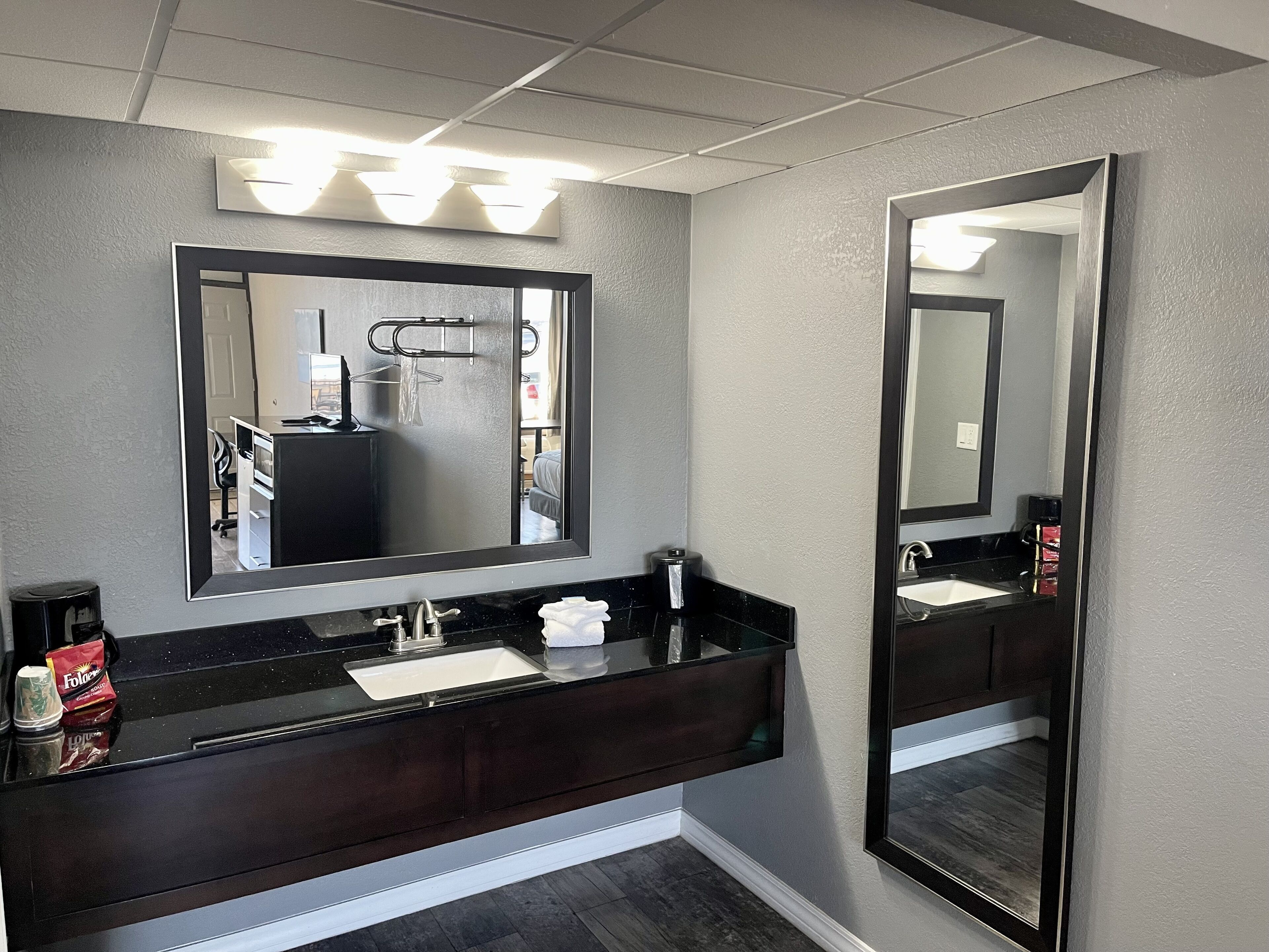 Un bagno moderno con un mobile lavabo scuro, uno specchio grande e una zona doccia visibile sullo sfondo.