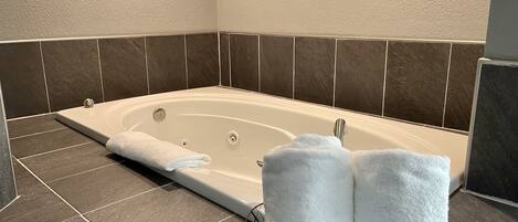 A modern bathroom with a freestanding bathtub, dark tiled walls, and a towel rack with two white towels.