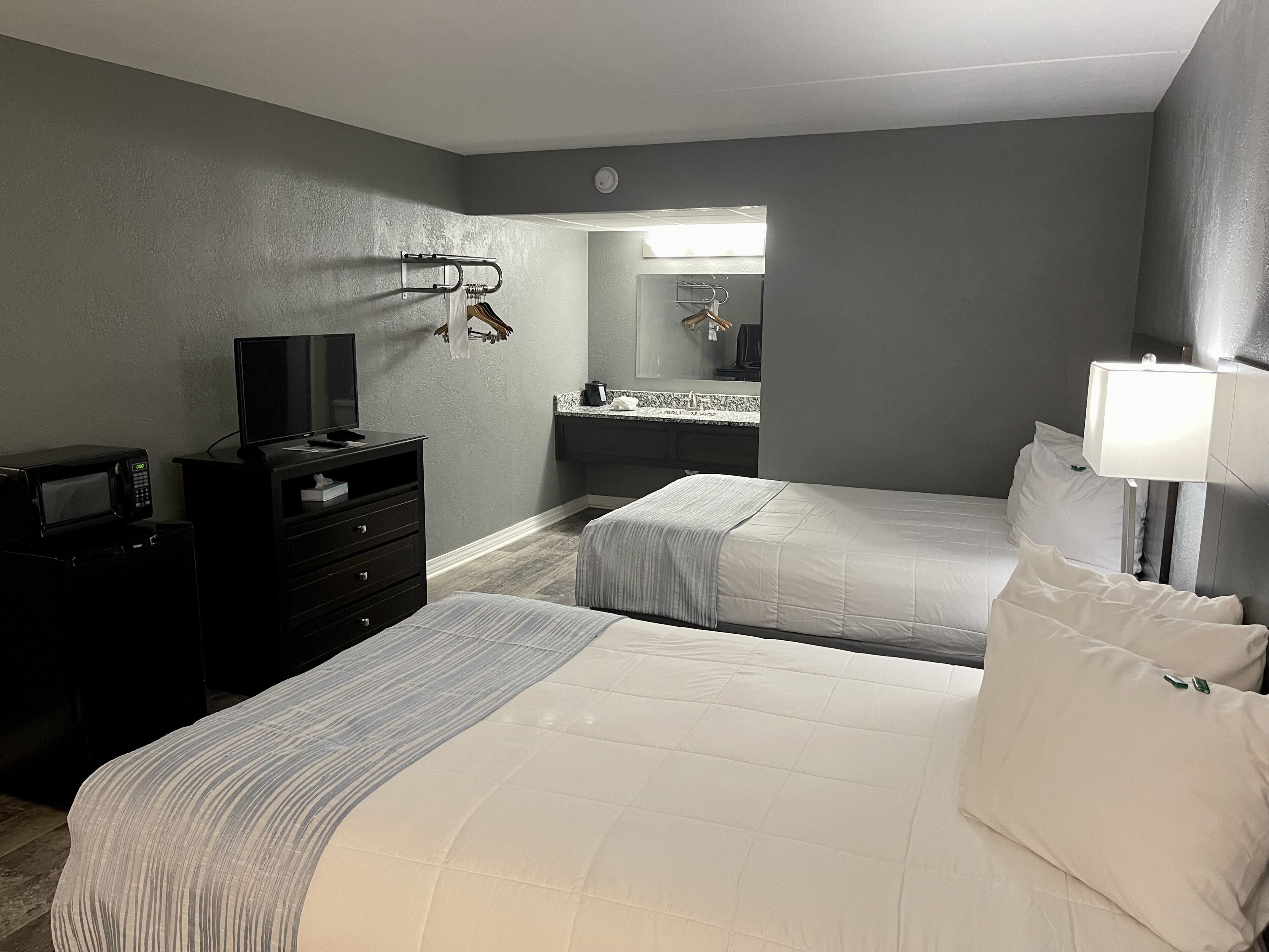 Habitación de hotel con dos camas, televisión, microondas, cómoda, espejo y baño visible a través de una puerta abierta.