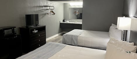 Habitación de hotel con dos camas, televisión, microondas, cómoda, espejo y baño visible a través de una puerta abierta.